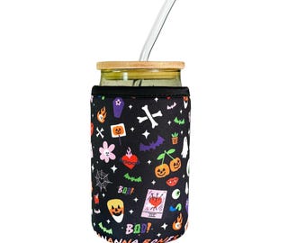 May include: A black and white reusable cup sleeve with a Halloween theme. The sleeve features a variety of spooky and cute illustrations, including pumpkins, bats, ghosts, and hearts. The text "BOO!" appears twice on the sleeve. The sleeve is made of neoprene and is designed to fit a standard 16 oz. cup.