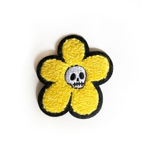 Könnte beinhalten: Gelber Filzblumen-Patch mit schwarzem Umriss und einem weißen Totenkopf in der Mitte.