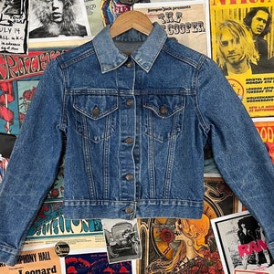 May include: A classic blue denim jacket with a button-up front, two chest pockets, and long sleeves. The jacket has a slightly cropped fit.