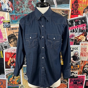 May include: A dark blue denim long-sleeved shirt with a pointed collar, button-down front, and two chest pockets with button closures.