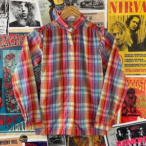 May include: A long-sleeved, button-up shirt with a rainbow plaid pattern. The shirt has ruffles on the shoulders and a white collar.