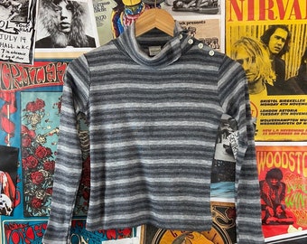 Könnte beinhalten: Ein graues und weiß gestreiftes Langarm-Rollkragen-Shirt mit einem Knopfdetail an der Schulter.