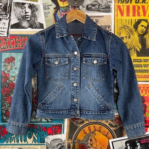 May include: A blue denim jacket with a button closure and two front pockets. The jacket has a classic style and is made of a durable material.