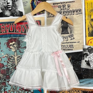 May include: White lace babydoll dress with a pink ribbon. The dress has a ruffled skirt and a lace trim.