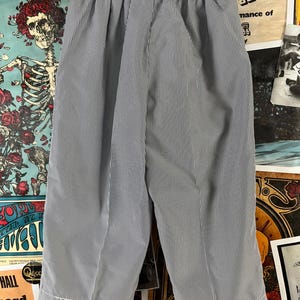 May include: A pair of blue and white striped shorts with an elastic waistband. The shorts have a vertical stripe pattern and are made of a lightweight fabric. The hem of the shorts is finished with a white trim.