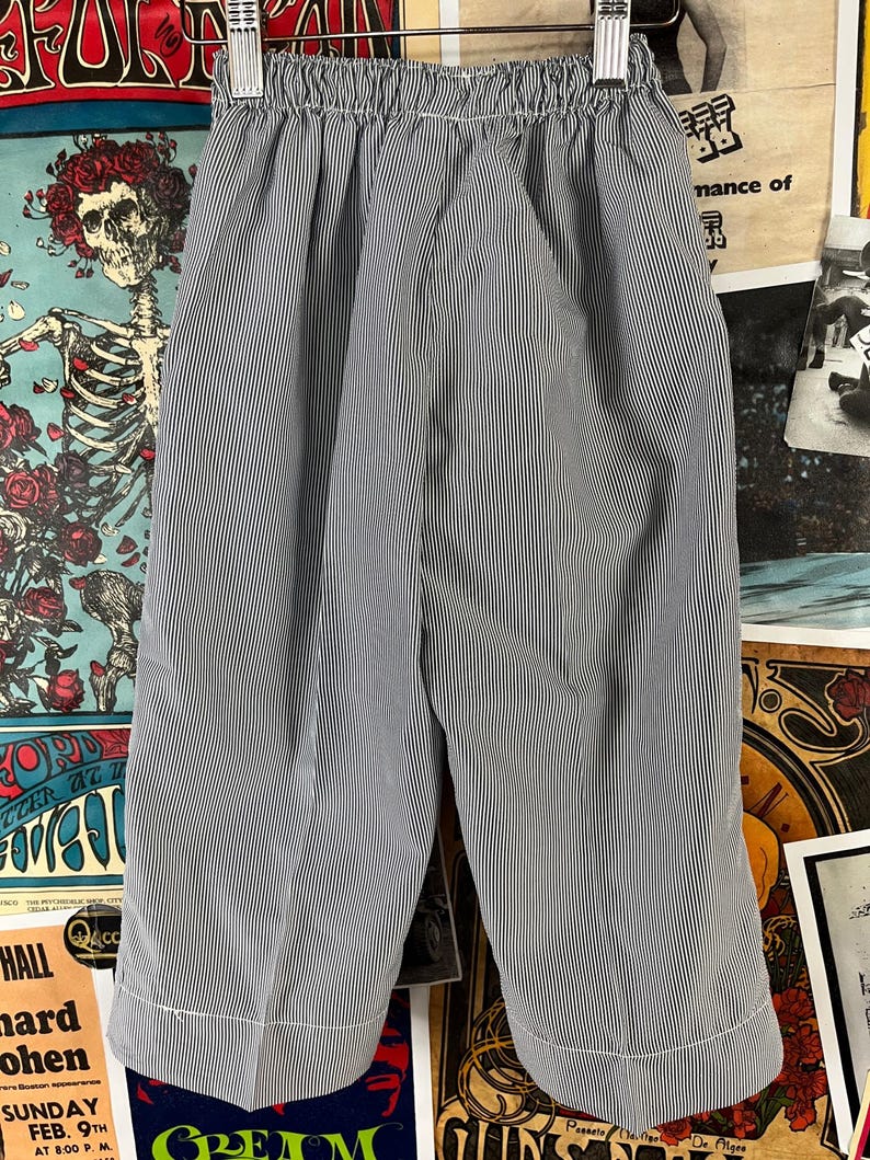 May include: A pair of blue and white striped shorts with an elastic waistband. The shorts have a vertical stripe pattern and are made of a lightweight fabric. The hem of the shorts is finished with a white trim.