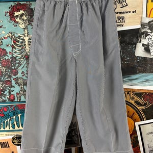 May include: Blue and white striped cropped pants with an elastic waistband. The pants have a vertical stripe pattern and are made of a lightweight fabric. The hem of the pants is finished with a white border. The pants are hanging on a hanger.