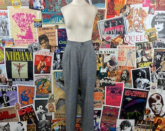May include: Gray tweed pants with a button fly and pleats. The pants are on a mannequin against a background of vintage concert posters.