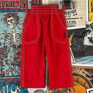 May include: Bright red corduroy pants with white stitching details. The pants have an elastic waistband and a small black tag. The style is casual and comfortable, suitable for everyday wear.