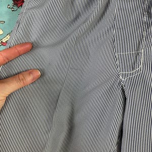 May include: Close-up of blue and white striped fabric. The fabric has a vertical stripe pattern with a pocket detail on the right side. The fabric is slightly wrinkled, suggesting it is made of a soft material.