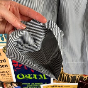 May include: Close-up of a sleeve cuff with a blue and white striped pattern. The cuff is folded back, revealing the inside lining and stitching. The fabric has a classic, tailored look.