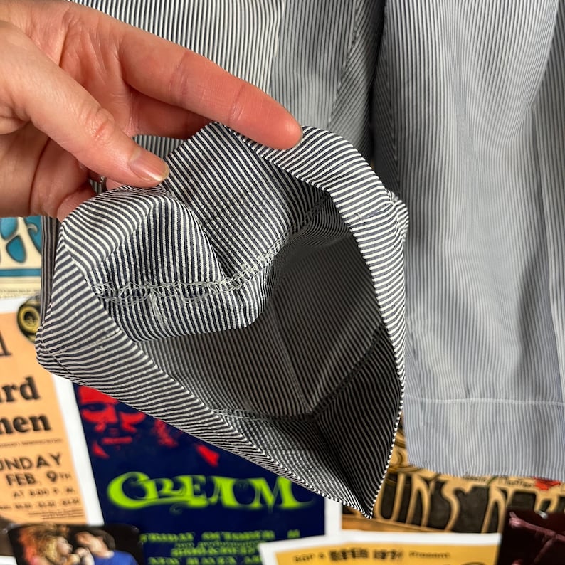 May include: Close-up of a sleeve cuff with a blue and white striped pattern. The cuff is folded back, revealing the inside lining and stitching. The fabric has a classic, tailored look.