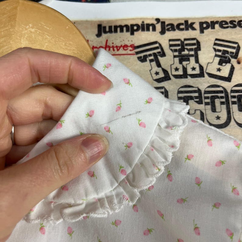 K&ouml;nnte beinhalten: Wei&szlig;e Baumwollbluse mit R&uuml;schenkragen und kleinem rosafarbenem Blumenmuster. Der Kragen hat einen gewellten Rand.