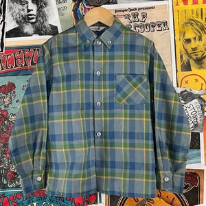 May include: A blue, green, and yellow plaid shirt with a button-down collar and a chest pocket. The long-sleeved shirt is displayed on a wooden hanger. The shirt's pattern is a classic check design.