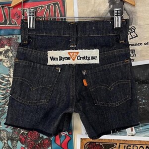 Peut inclure: Short en jean bleu foncé avec ourlet effiloché. Le short a un patch au dos qui indique "Van Dyne Crotty, Inc."