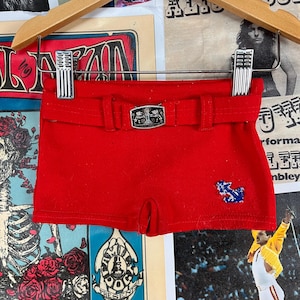 Op de afbeelding: Rode shorts met een zilveren gespsluiting en een blauw-wit ankerontwerp.
