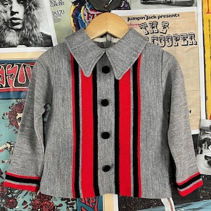 Puede incluir: Una camisa gris con botones y rayas rojas y negras. La camisa tiene cuello y mangas largas.
