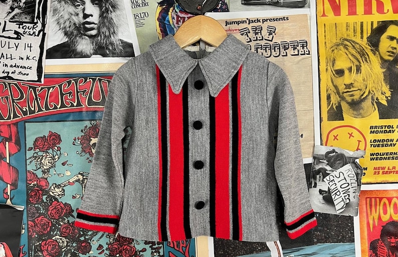 Puede incluir: Una camisa gris con botones y rayas rojas y negras. La camisa tiene cuello y mangas largas.