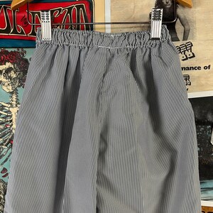 May include: Blue and white striped shorts with an elastic waistband. The shorts are hanging on a metal hanger. The fabric has vertical stripes. The shorts are made of a lightweight material.