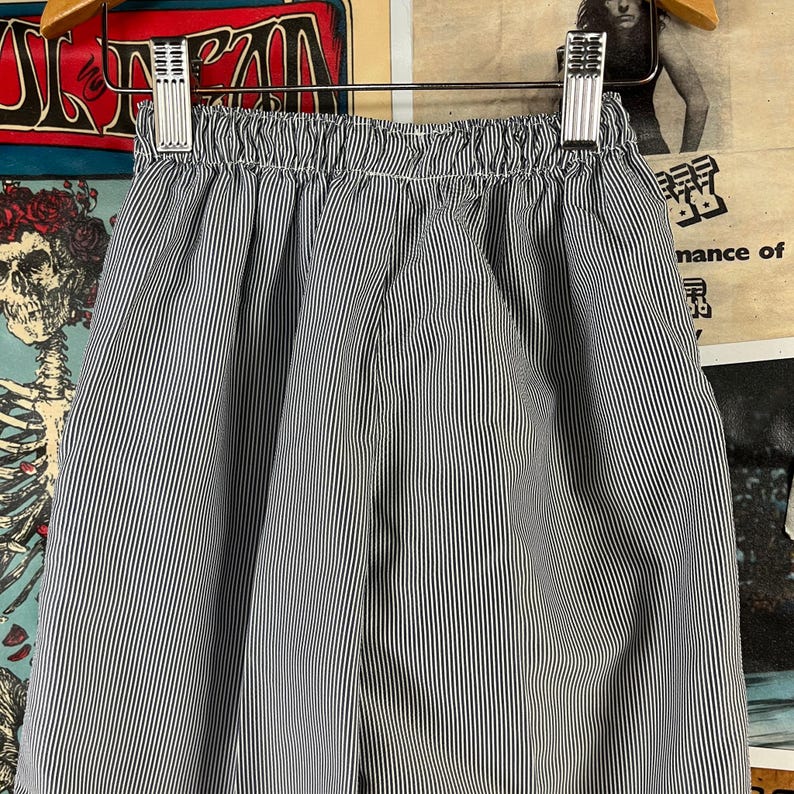 May include: Blue and white striped shorts with an elastic waistband. The shorts are hanging on a metal hanger. The fabric has vertical stripes. The shorts are made of a lightweight material.
