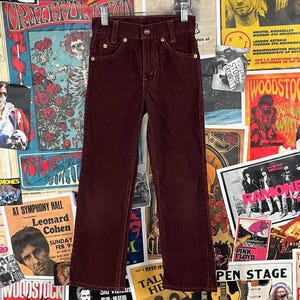 May include: A pair of burgundy corduroy trousers with a straight leg fit. The trousers have a button fly and belt loops.