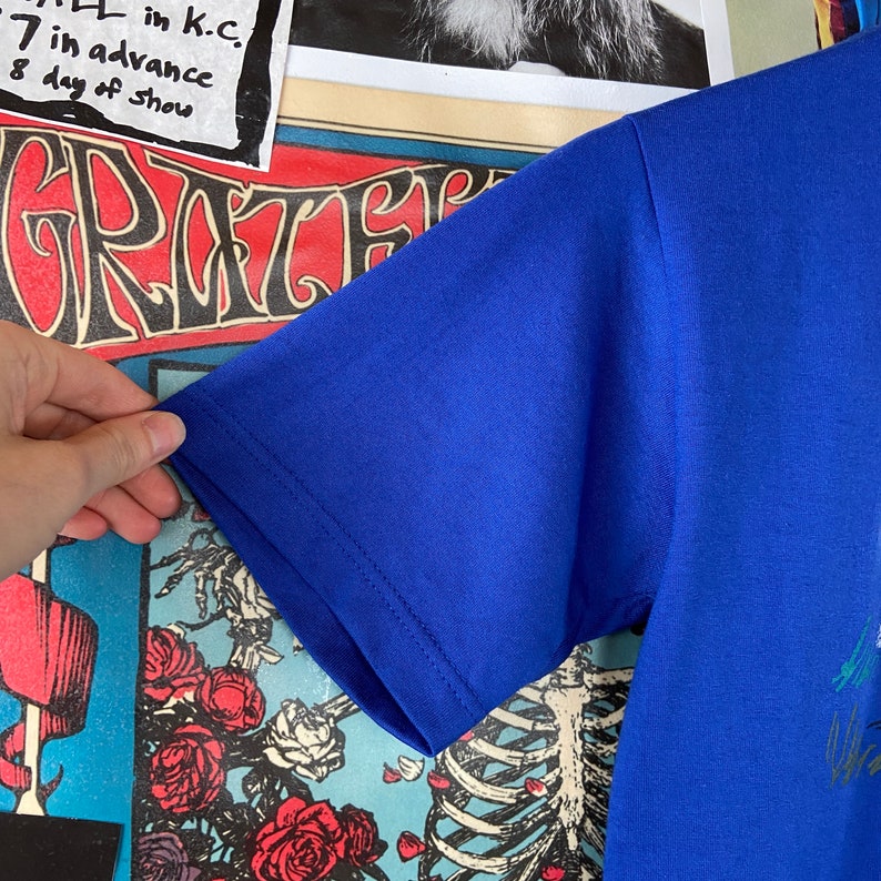 K&ouml;nnte beinhalten: Ein kurz&auml;rmliges T-Shirt in Royalblau mit einem grafischen Druck. Der Druck zeigt ein farbenfrohes Design mit einem Skelett und Blumen.