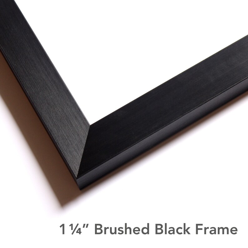 Puede incluir: Una secci&oacute;n de esquina de un marco de fotos con un acabado negro cepillado. El marco tiene una uni&oacute;n en inglete y un perfil plano. El texto impreso debajo del marco dice 1 1/4" Brushed Black Frame, indicando el ancho del borde.
