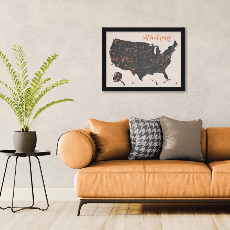 May include: A framed map of the United States, featuring a dark gray silhouette of the country with red markers indicating national parks. The words "national parks" are written in a cursive font above the map. The frame is black.