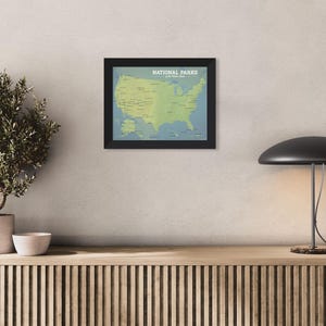 May include: A framed map of the United States, showing National Parks in green on a blue backdrop. The map is in a black frame and is mounted on a neutral wall. The text "NATIONAL PARKS" is at the top.