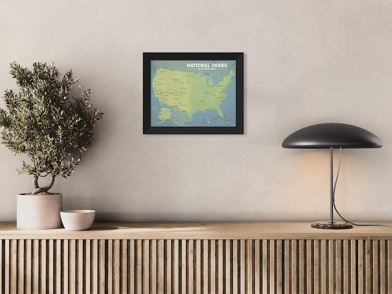 May include: A framed map of the United States, showing National Parks in green on a blue backdrop. The map is in a black frame and is mounted on a neutral wall. The text "NATIONAL PARKS" is at the top.