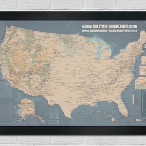 May include: A framed map of the United States, showcasing national parks, forests, and conservation areas. The map features a detailed depiction of the country's geography, with various colors and symbols indicating different locations. The frame is black.
