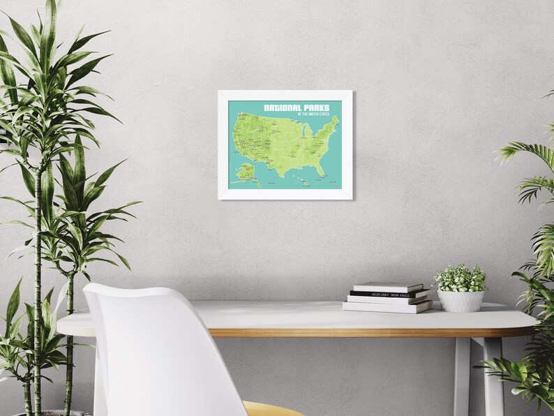 May include: A framed map of the United States National Parks. The map is green on a teal background, with the text "NATIONAL PARKS of the UNITED STATES" at the top. The frame is white. The map is hanging on a light grey wall.