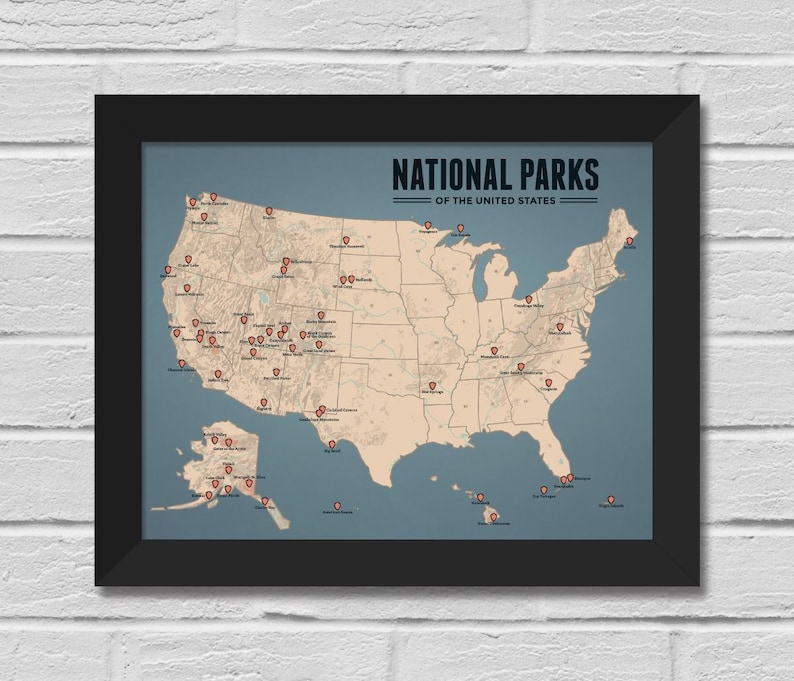 May include: Framed map of the United States National Parks. The map is in a black frame, with a blue-grey background. The map itself is a beige colour, with red pin markers indicating the locations of the parks. The text "NATIONAL PARKS OF THE UNITED STATES" is at the top.