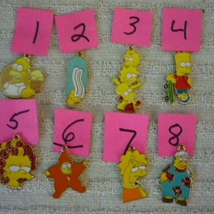 Może przedstawiać: Osiem żółtych figurek z kreskówek z różnymi pozami i wyrażeniami twarzy. Figurki są ponumerowane od 1 do 8 na różowych kwadratach papieru. Figurki są wykonane z metalu i mają złote wykończenie.