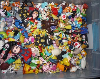 May include: A clear plastic container filled with a variety of colorful plastic figurines. The figurines are mostly cartoon characters and animals, and they are all different sizes and shapes.