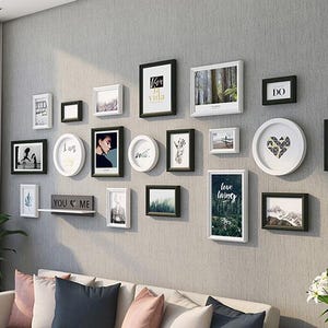 May include: A gallery wall arrangement featuring a collection of rectangular and circular picture frames in black and white finishes. The frames display various photographs, illustrations, and text prints, including the phrases "la vida", "I am", "DO", "love living", and "YOU ME".