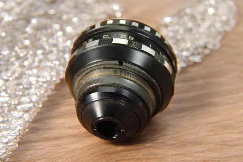 May include: A black camera lens with a silver ring and markings that read "0.7 0.8".