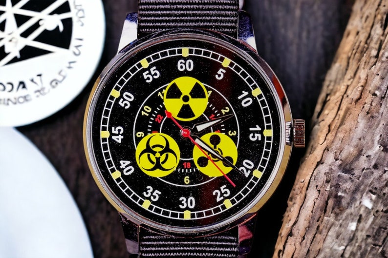 May include: A black wristwatch with a silver case and a black fabric band. The watch face features yellow radiation symbols and a red second hand. The numbers are white and yellow.