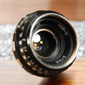 May include: A black camera lens with a silver ring and the text "МИР-11" and "2/135" printed on it.