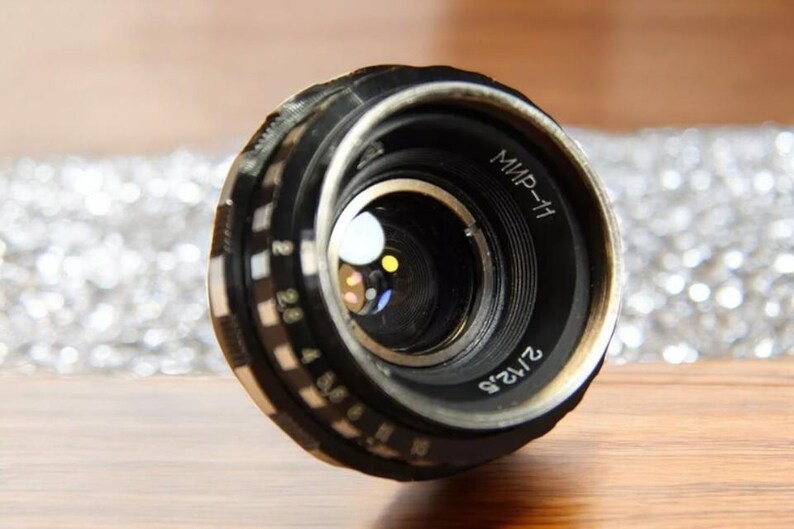 May include: A black camera lens with a silver ring and the text "МИР-11" and "2/135" printed on it.