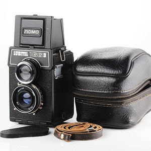 May include: A black Lubitel 166B medium format film camera with a LOMO logo on the top. The camera is in a black leather case with a brown leather strap.