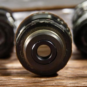 May include: Three black camera lens caps with a silver ring around the opening. The lens caps are on a wooden surface.