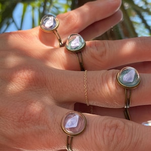 Può includere: Quattro anelli d'oro con cupole di vetro trasparente che contengono piccoli cristalli viola. Gli anelli sono indossati sulle dita di una persona.