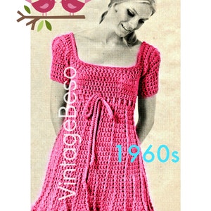 Puede incluir: Un patrón de vestido vintage de ganchillo de la década de 1960. El vestido es rosa y tiene un escote cuadrado, mangas cortas y un lazo en la cintura. El patrón es para un vestido que llega a la rodilla y tiene una falda acampanada.