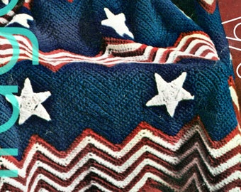 May include: A crocheted blanket in red, white, and blue with a chevron pattern and white stars. The blanket is folded and draped over a chair. The text "1970s" is visible in the upper right corner of the image.