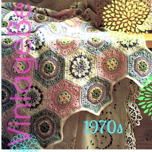 May include: A crocheted blanket with a hexagonal pattern in shades of pink, blue, green, and white. The blanket is draped over a white lace tablecloth with the text "1970s" in blue lettering. The blanket is a vintage design.