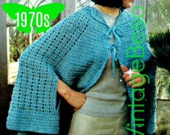 Könnte beinhalten: Ein hellblauer Häkelumhang mit einer Binde zum Verschließen. Der Umhang hat eine Kapuze und wird von einer Person mit kurzen, dunklen Haaren getragen. Das Bild enthält den Text "1970s" in Grün.
