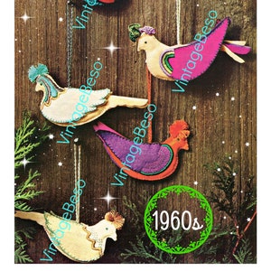 Op de afbeelding: Vijf kleurrijke vilt vogelversieringen met een ontwerp uit de jaren 1960. De vogels zijn allemaal in verschillende kleuren en hebben verschillende patronen. Ze hangen aan een houten achtergrond.
