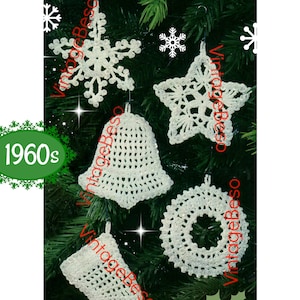 Könnte beinhalten: Fünf weiße gehäkelte Weihnachtsornamente hängen an einem grünen Weihnachtsbaum. Die Ornamente sind ein Schneeflocke, ein Stern, eine Glocke, ein Kranz und ein Strumpf.