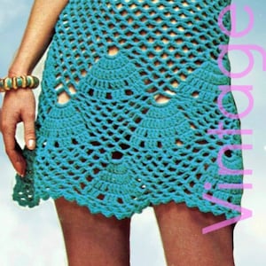 May include: A turquoise crochet dress with a scalloped hem and openwork design. The image has text that says "1970s" and "Vintage Goods". The dress is sleeveless and appears to be a mini dress.